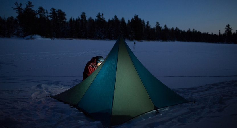 a tent resting on a snowy landscape is illuminated by a person's headlamp